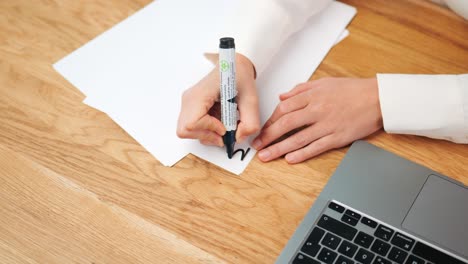 Woman-hand-drawing-with-black-pen-on-sheet-of-paper-at-modern-desk-in-the-office