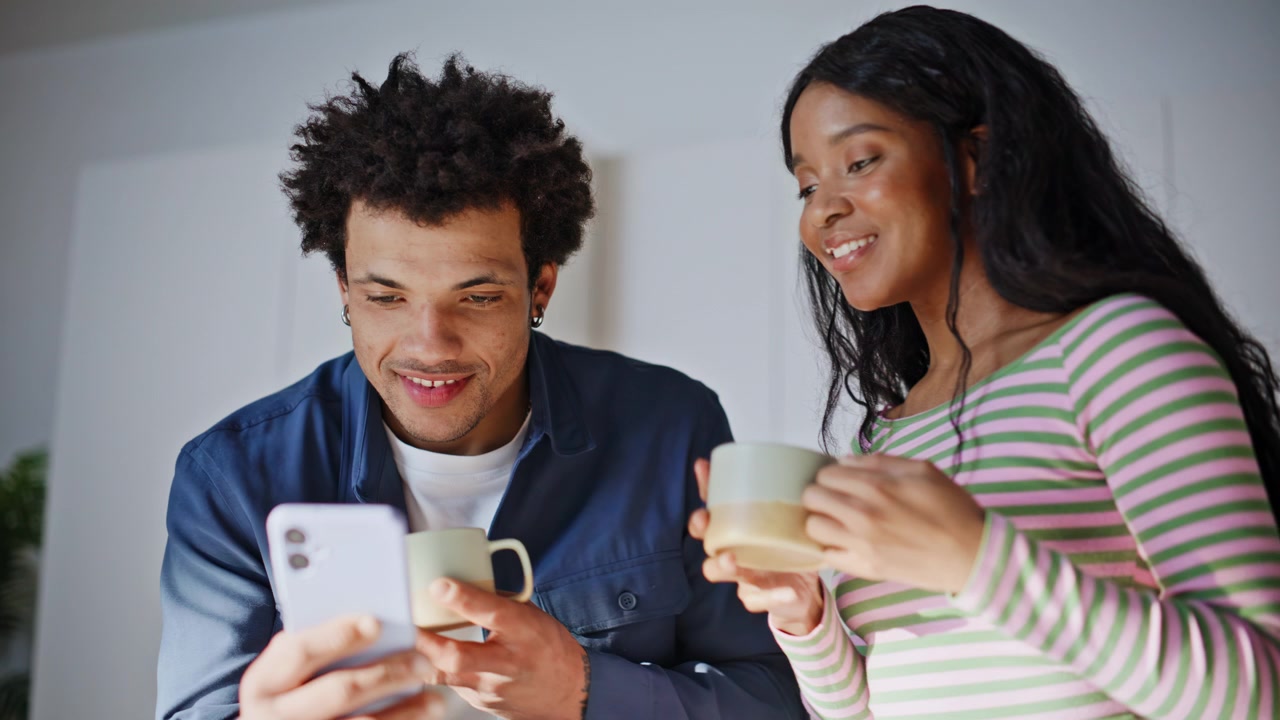 Gentle wife bringing tea to relaxed husband holding smartphone kitchen closeup