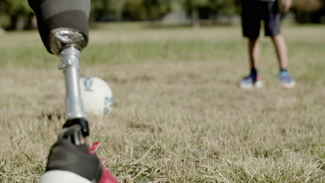 primer plano de la pierna protésica del hombre pateando la pelota en el césped