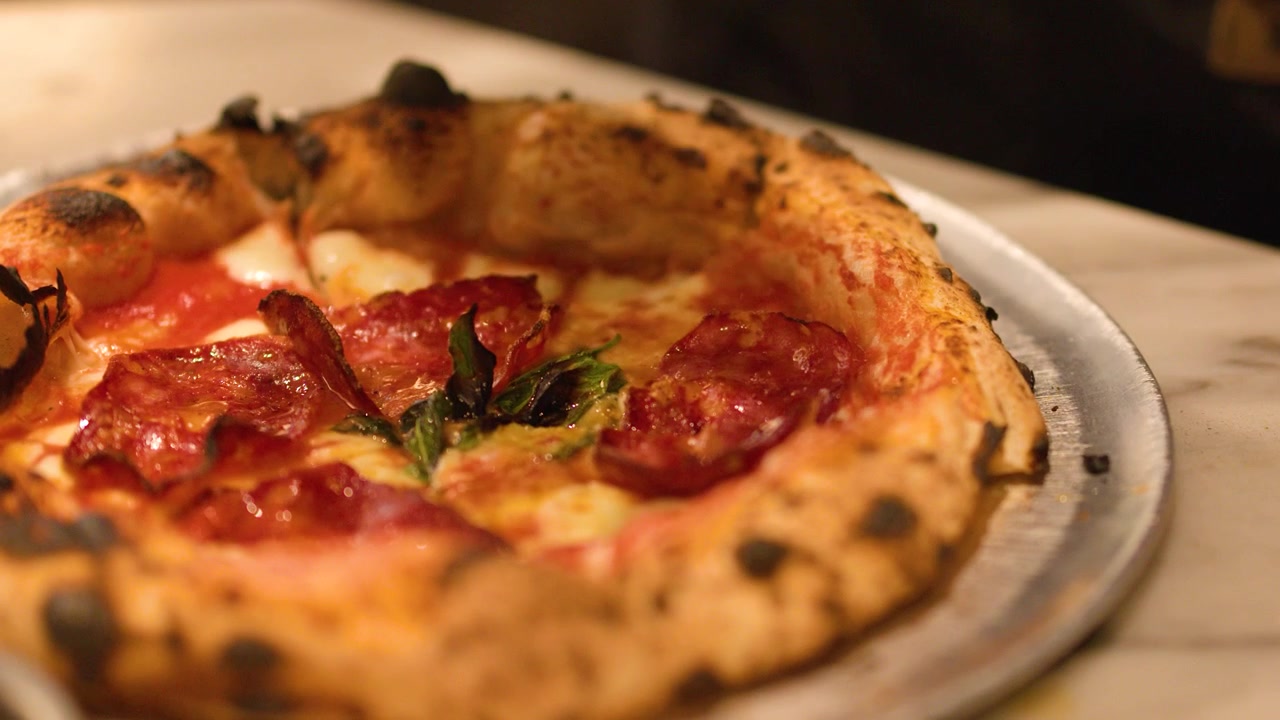 Primo piano di uno chef che irrora olio su una pizza gourmet con crosta carbonizzata in una cucina professionale
