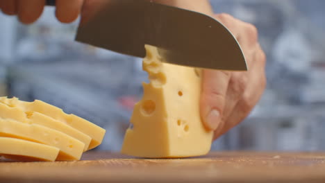 corta el queso amarillo en un tablero de madera de cerca.