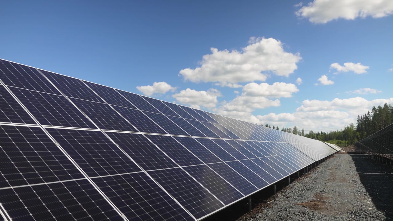 Painéis solares alinhados em um parque solar capturando a luz solar, energia renovável eficiente em paisagem verde, rastreamento lento e médio para a esquerda com reflexo de nuvens.