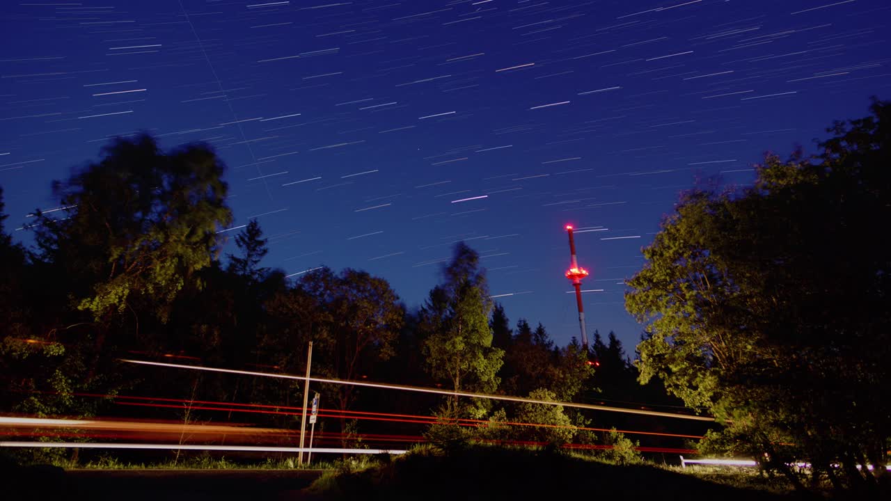 밤에는 빨간색으로 조명된 라디오 타워로 독일 숲 위에 움직이는 별과 스타트레일