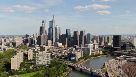 High-aerial-backward-flying-drone-shot-with-beautiful-Philadelphia-cityscape-on-a-bright-summer-sunny-day-with-blue-skies-and-puffy-clouds