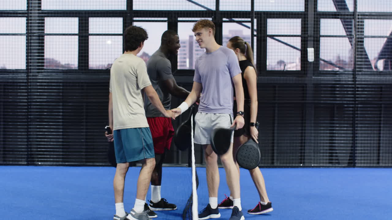 Group of diverse friends on padel court holding rackets, enjoying friendly conversation