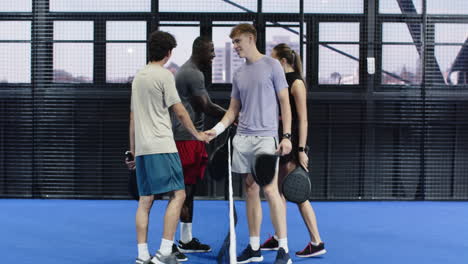 group of diverse friends on padel court holding rackets, enjoying friendly conversation