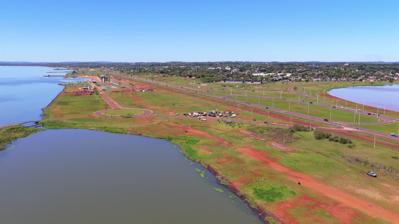 Miguel Lanus and Acceso Sur in Posadas, Misiones featuring sprawling fields bordered by the Paraná River and distinctive red earth, with roads and highways curving along the waterfront, drone shot