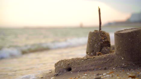 Meereswellen,-Die-Bei-Sonnenuntergang-An-Einem-Sandstrand-Auf-Eine-Sandburg-Krachen