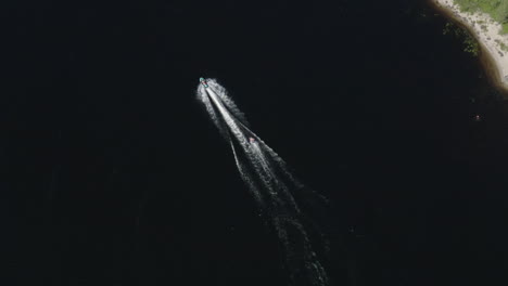 aerial wide view of a ringo ride behind a fast jetski in deep dark water in a river in sweden