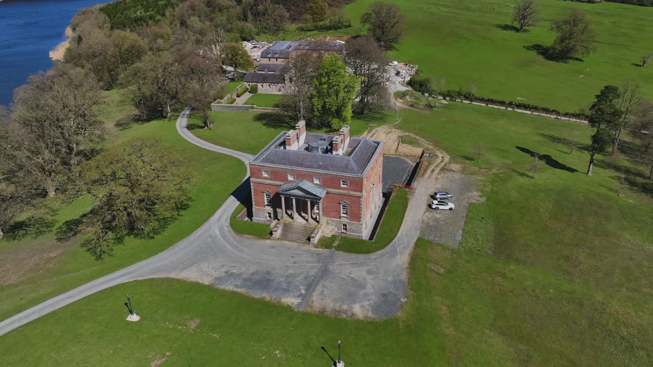 Bellamont House, County Cavan, Ireland, April 2023. Drone orbiting counterclockwise over historic red-brick mansion, nature, serene green landscape on sunny day.