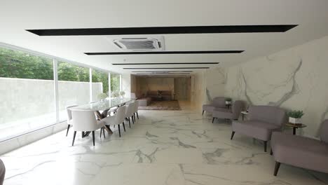 sala de reuniones blanca con decoración de patrón de mármol, amueblada con larga mesa de vidrio, sillones grises y blancos