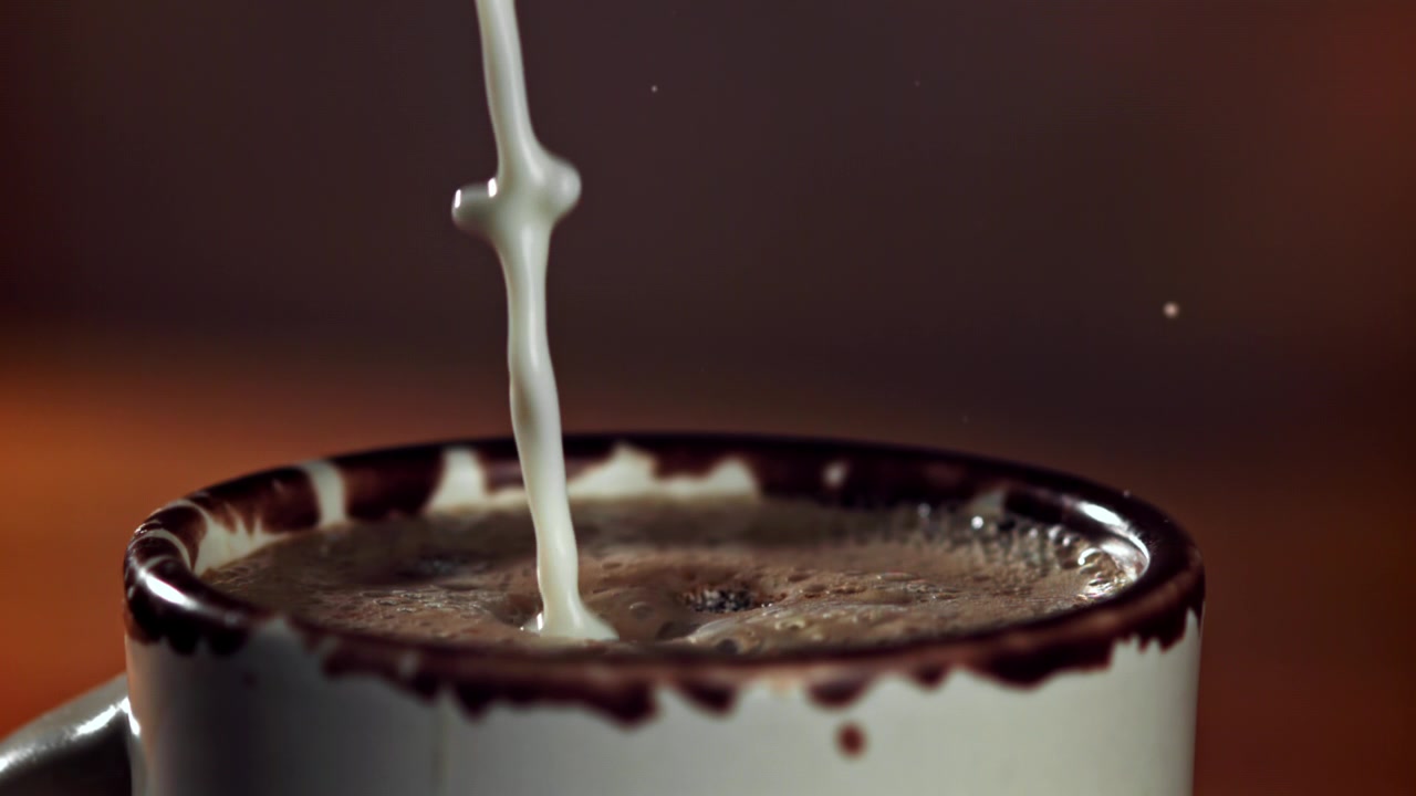 Versamento di latte al rallentatore nel caffè caldo in una tazza