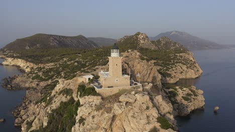 Un-Punto-De-Interés-De-Un-Dron-Giratorio-De-Un-Faro-En-El-Borde-De-Unos-Altos-Acantilados,-Con-La-Bandera-Griega-En-Un-Lado