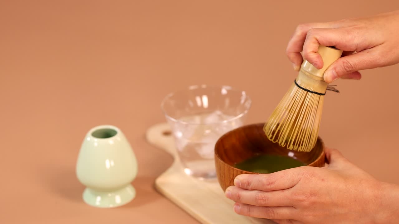 Hands whisking matcha green tea in wooden bowl, soft lighting, minimal background, steady camera
