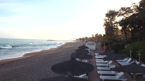 Luftaufnahme-Des-Strandes-Bei-Sonnenuntergang-In-Marbella,-Flug-über-Sonnenschirme-Am-Perfekten-Strand,-Erstaunlicher-Luxus-Lebensstil