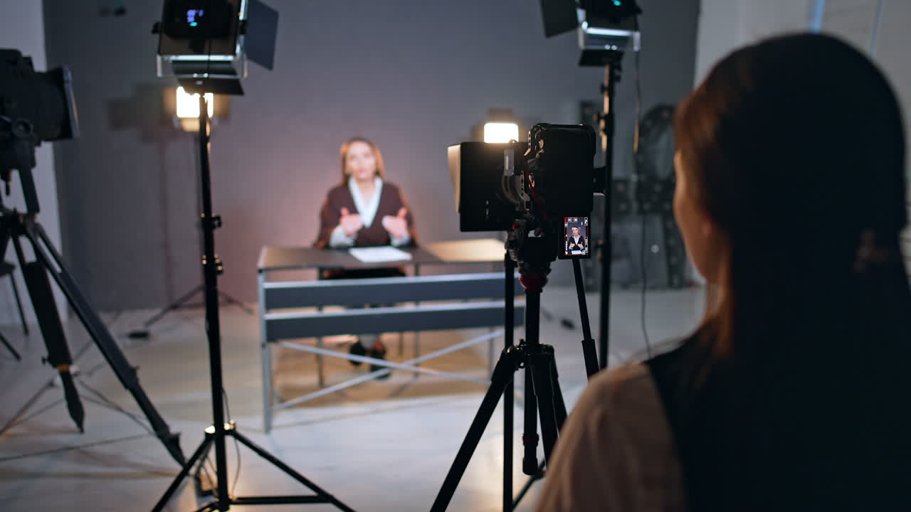 Unrecognized brunette lady standing backstage in photo studio. Female reporter talks for video at blurred backdrop.