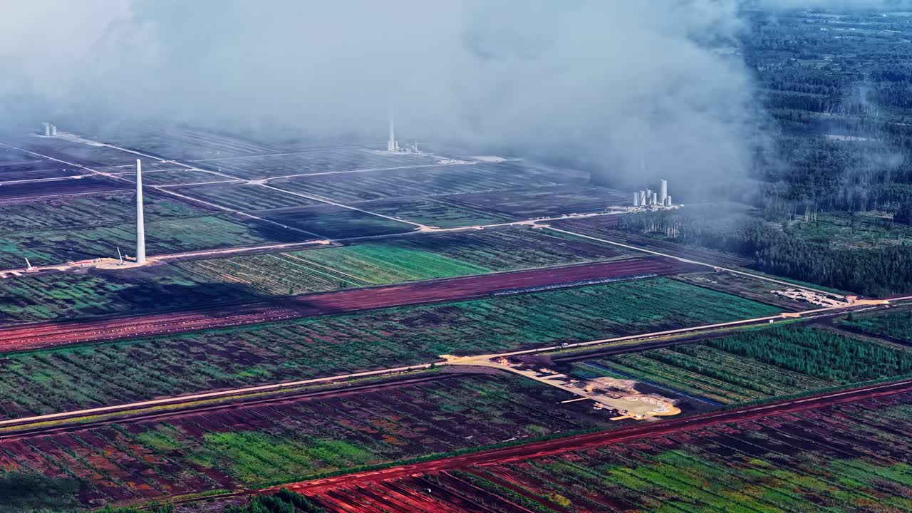 Drone shot of massive renewable energy project in Latvia showing installed wind turbine towers and active heavy-duty cranes at a construction site in the rural landscape