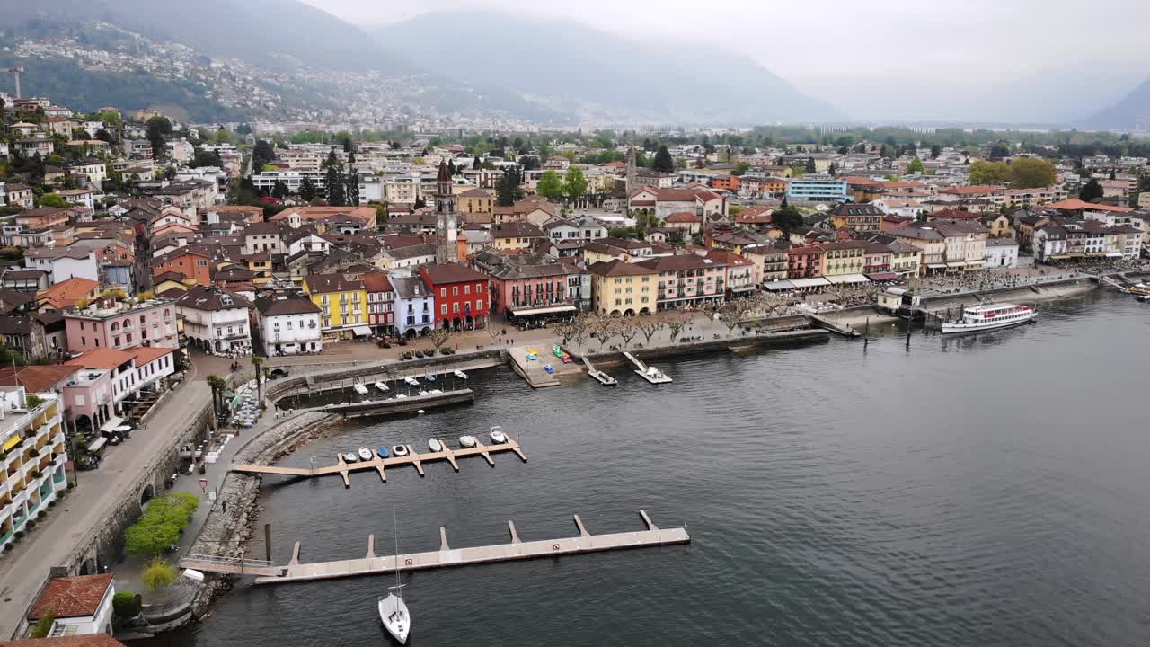 sobrevuelo aéreo sobre las orillas del lago maggiore hacia los tejados de ascona en ticino, suiza, con vistas al paseo junto al lago, los barcos y la torre de la iglesia