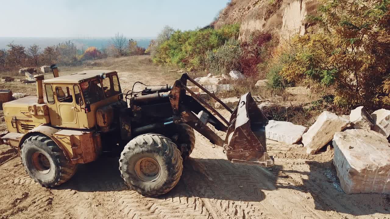 professional bulldozer with a bucket is picking up stones on sandy quarry against the backdrop of wild nature. Close-up