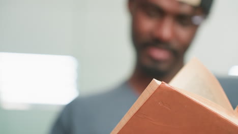 close up of student flipping through brown hardcover in quiet library, hands holding book with shallow focus, soft motion blur on fingers, teal shelves in background