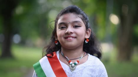 a cute little indian girl is smiling and laughing at the camera wearing indian tricolor flag, closeup, slow motion