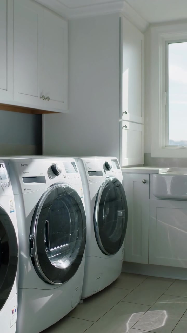 Vertical video: Shifting sunlight crossing washer and dryer in laundry, moving reflection on floor