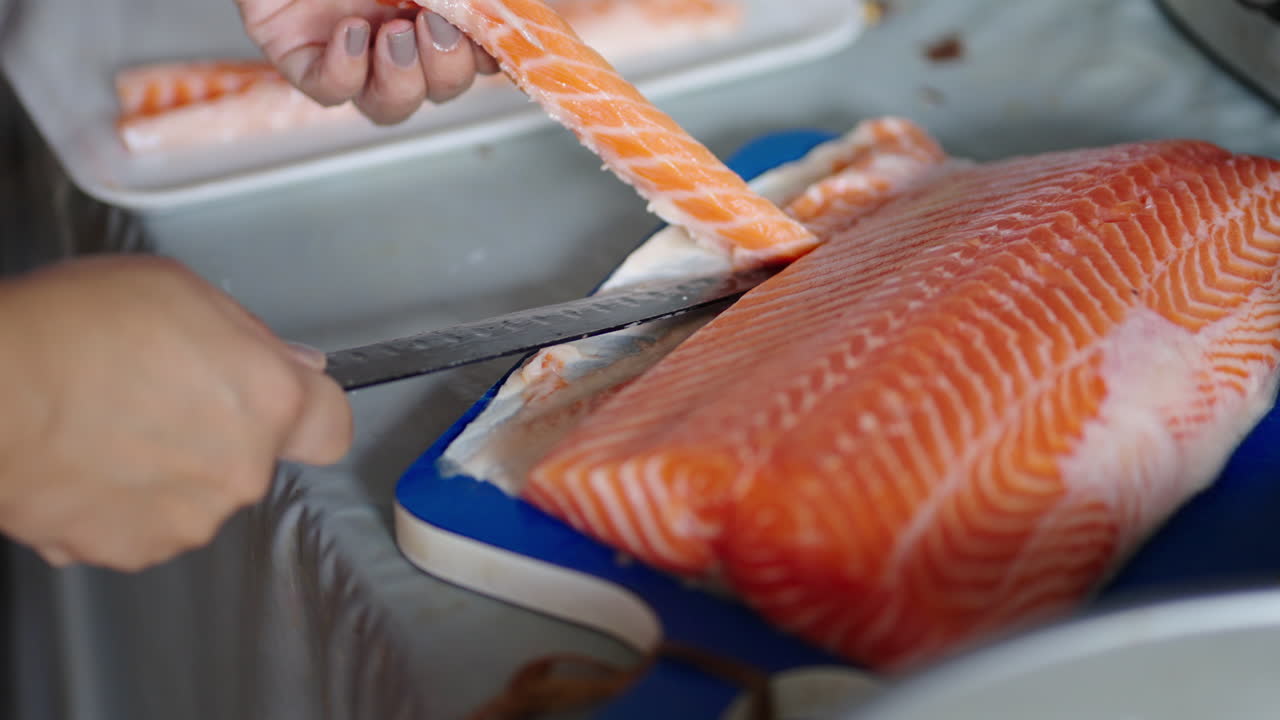 Chef slices strips of fresh raw salmon for making sushi, close up