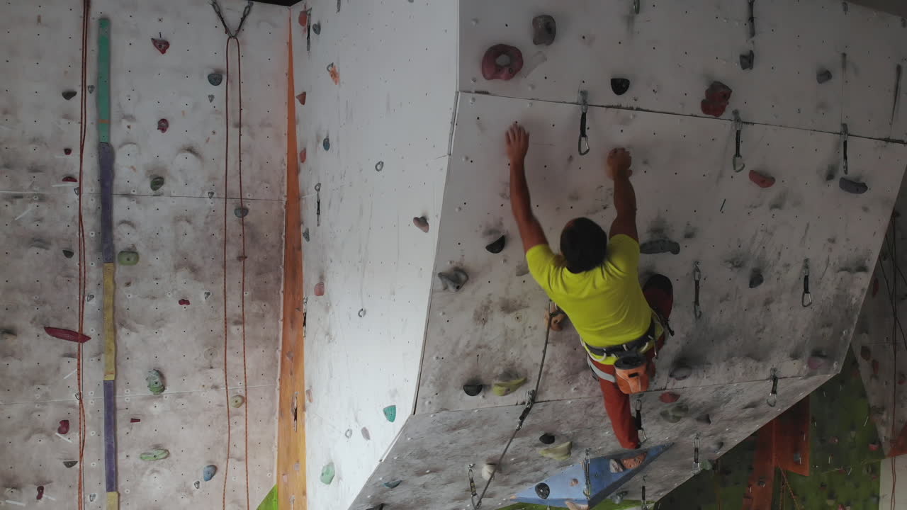 Young man Rock climber is Climbing At Inside climbing Gym. slim pretty man Exercising At Indoor Climbing Gym Wall.