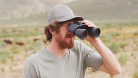 Bearded-caucasian-male-survivalist-looking-to-distance-with-binoculars-in-wilderness