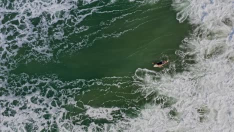 aerial: surfer duck diving technique under large breaking wave, bird's eye view