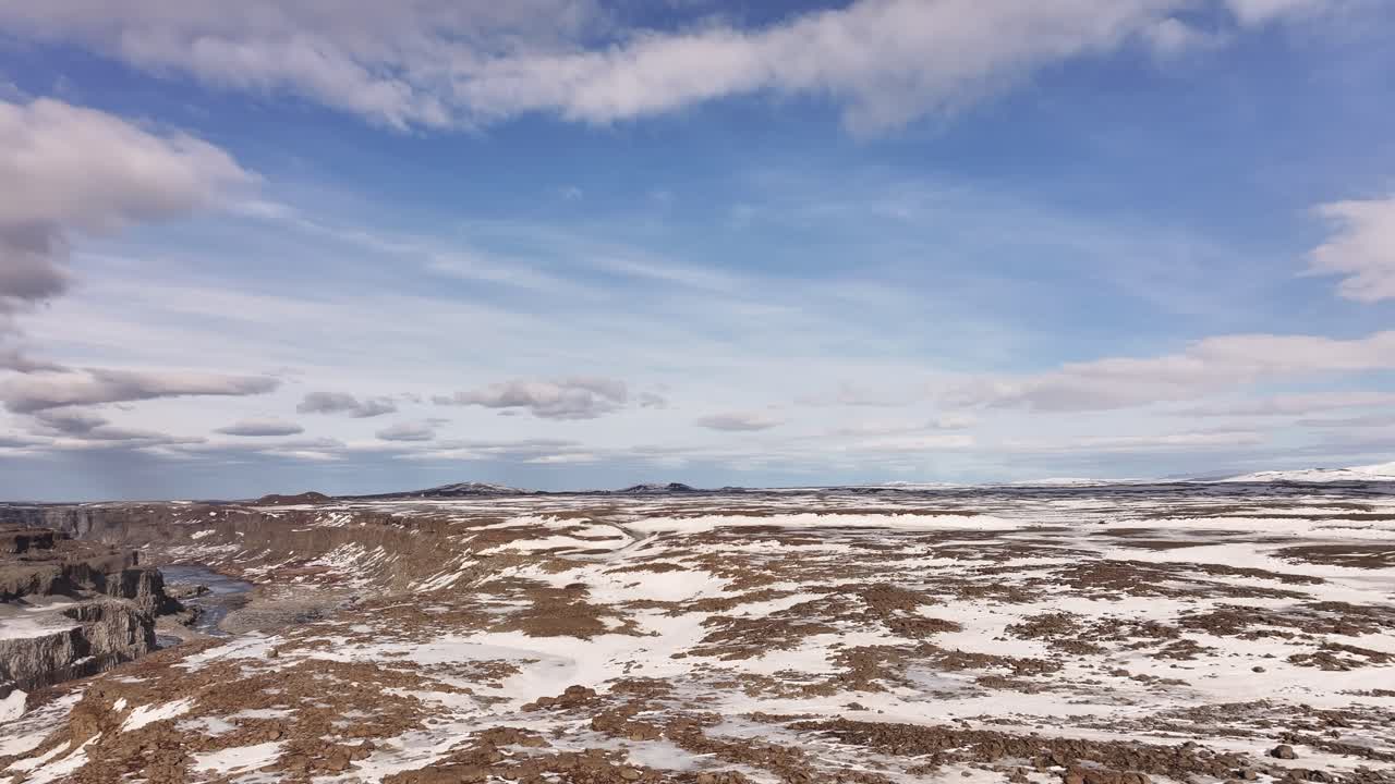 Bleak and expansive Icelandic winter landscape stretches under a pale sky, with frozen earth and barren volcanic terrain evoking isolation and the raw power of untouched nature.