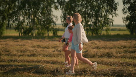 child walks with her two aunts through vast open field, one aunt holding rope and pointing towards something in distance, while trees form a lush green background, all enjoying outdoor stroll
