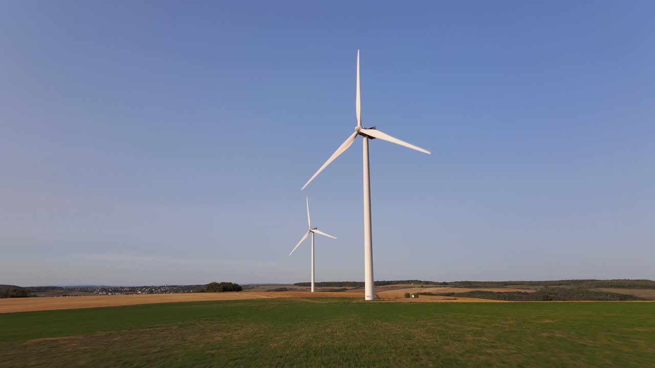 дрон летит к двум изолированным ветряным мельницам, вращающимся под голубым небом.