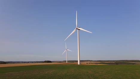 drone flying towards two isolated windmills spinning under blue sky