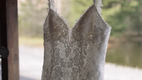 precioso vestido de novia colgado en una estructura de madera fuera de un lugar para celebrar bodas con un bokeh de árboles en el fondo