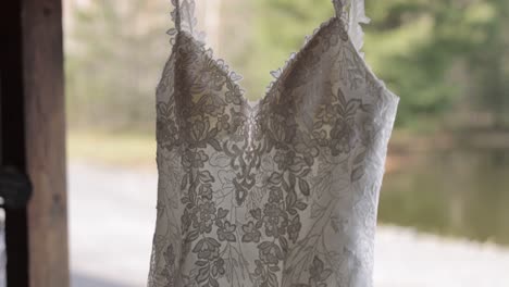 gorgeous wedding gown hanging on a wooden structure outside a wedding venue with bokeh of trees in the background