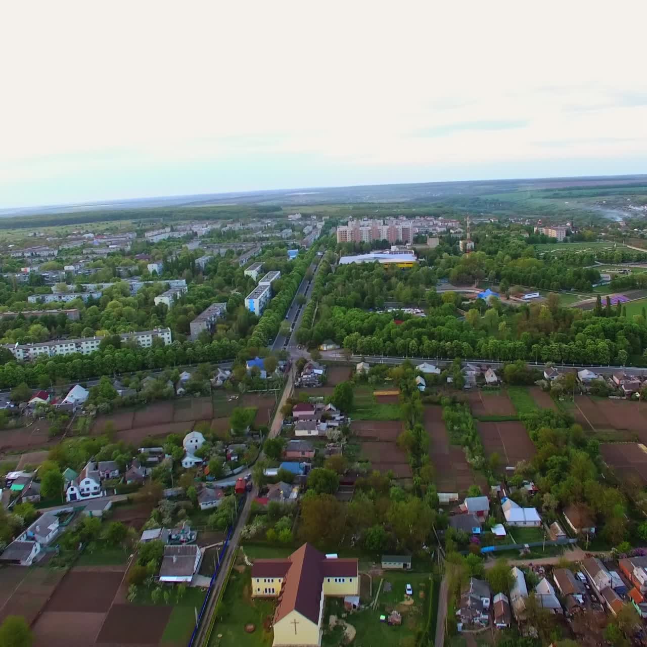 Peaceful little town panorama at daytime. Private houses neighboring farmlands and blocks of flats in the green area