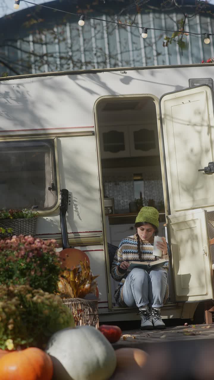 Woman reading a book in a camper van, autumn scene