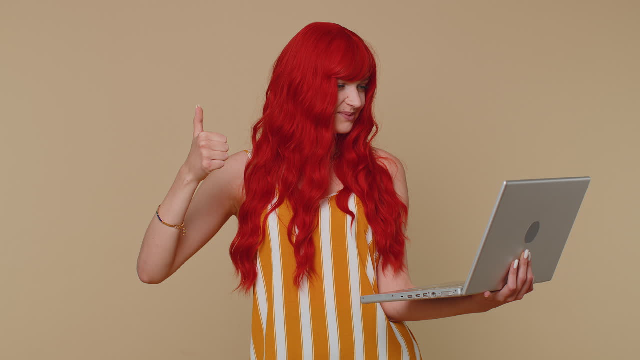 노트북에서 온라인에서 일하는 빨간 머리 소녀는 엄지손가락을 보여주고 긍정적인 좋은 피드백, 예를 들어, 복권 우승