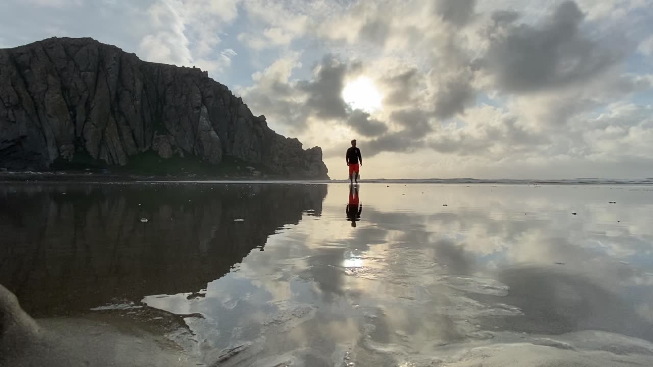 캘리포니아의 모로 베이 해변에서 산책하는 남자, 모로 베이의 상징적인 바위, 물 반사