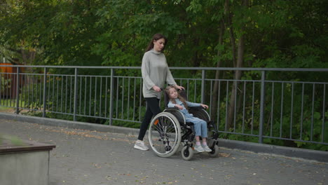 little girl rests in wheelchair pushed by mother in park