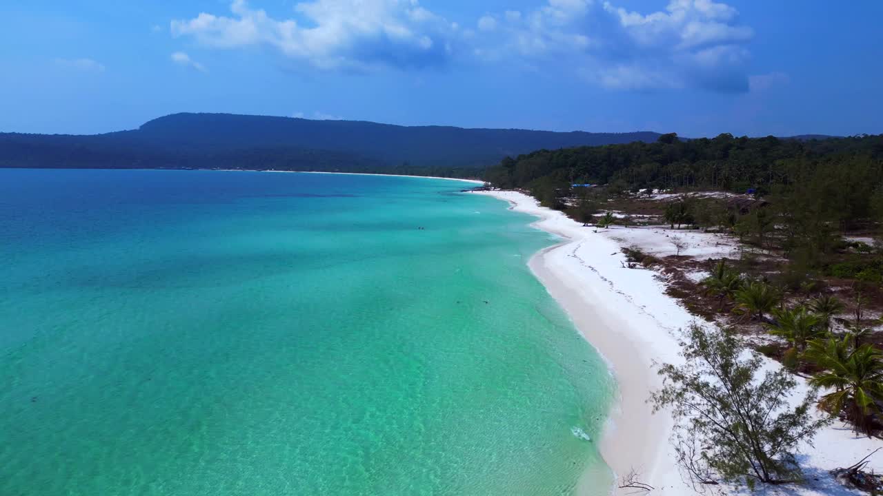 Sok San Beach with turquoise water washing the white sand, surrounded by palm trees and tropical vegetation. Tremendous aerial view flight ascending drone