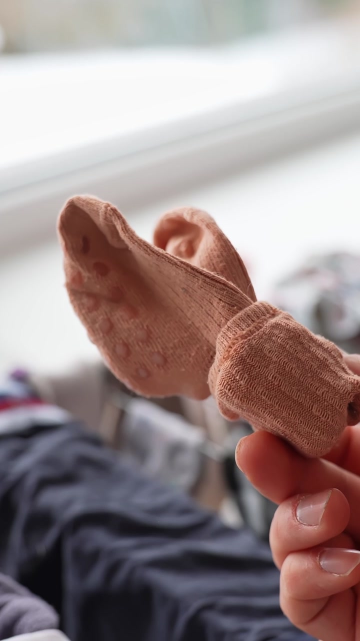 Hand tosses a beige sock toward a laundry basket in soft-focus background, showing home cleaning and organization routine. Vertical close-up b-roll.