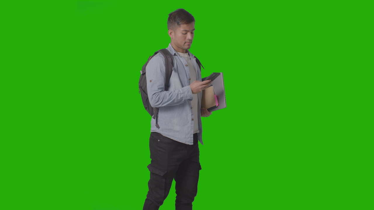 Three Quarter Length Shot Of Male University Or College Student Looking At Mobile Phone Against Green Screen 1