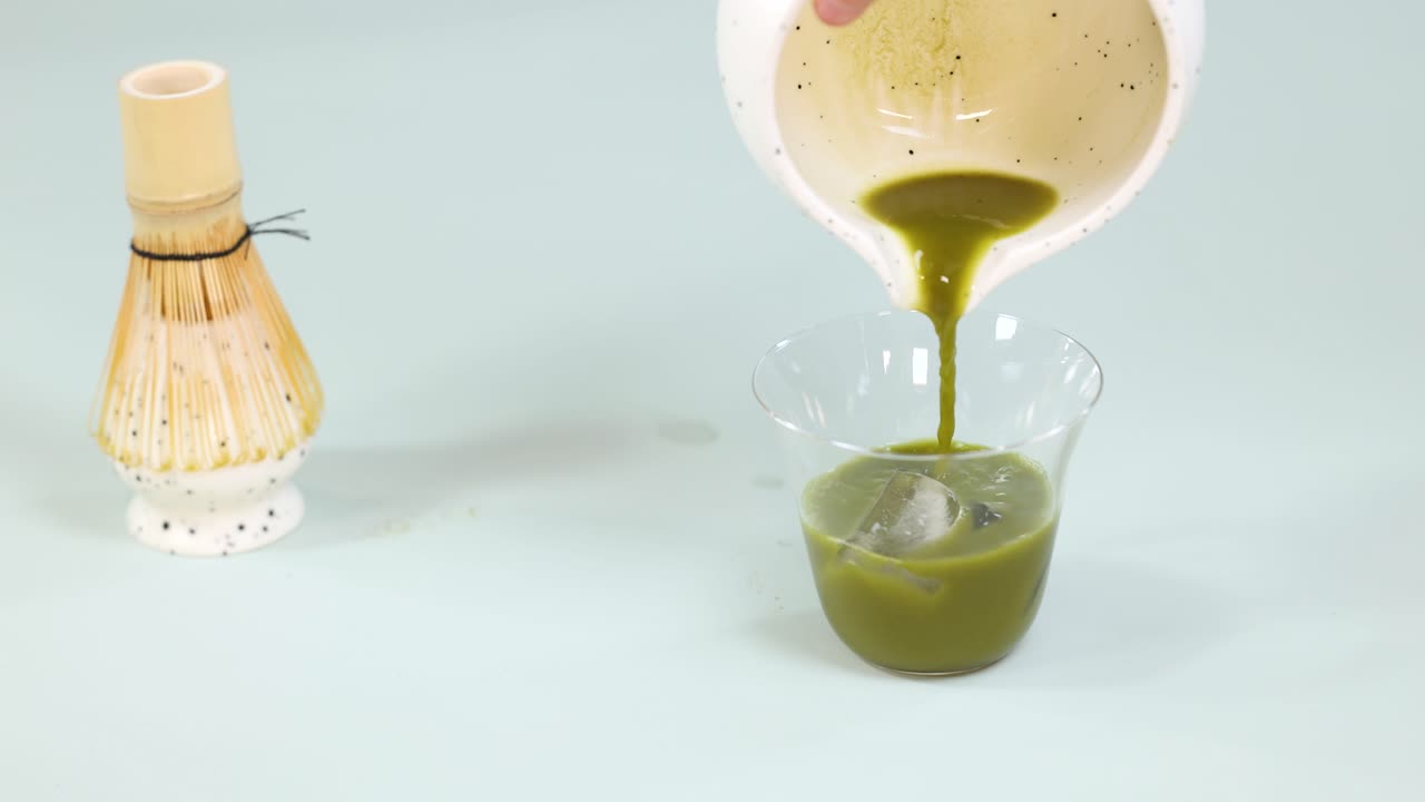 Iced matcha green tea in a glass with bamboo whisk, under bright lighting