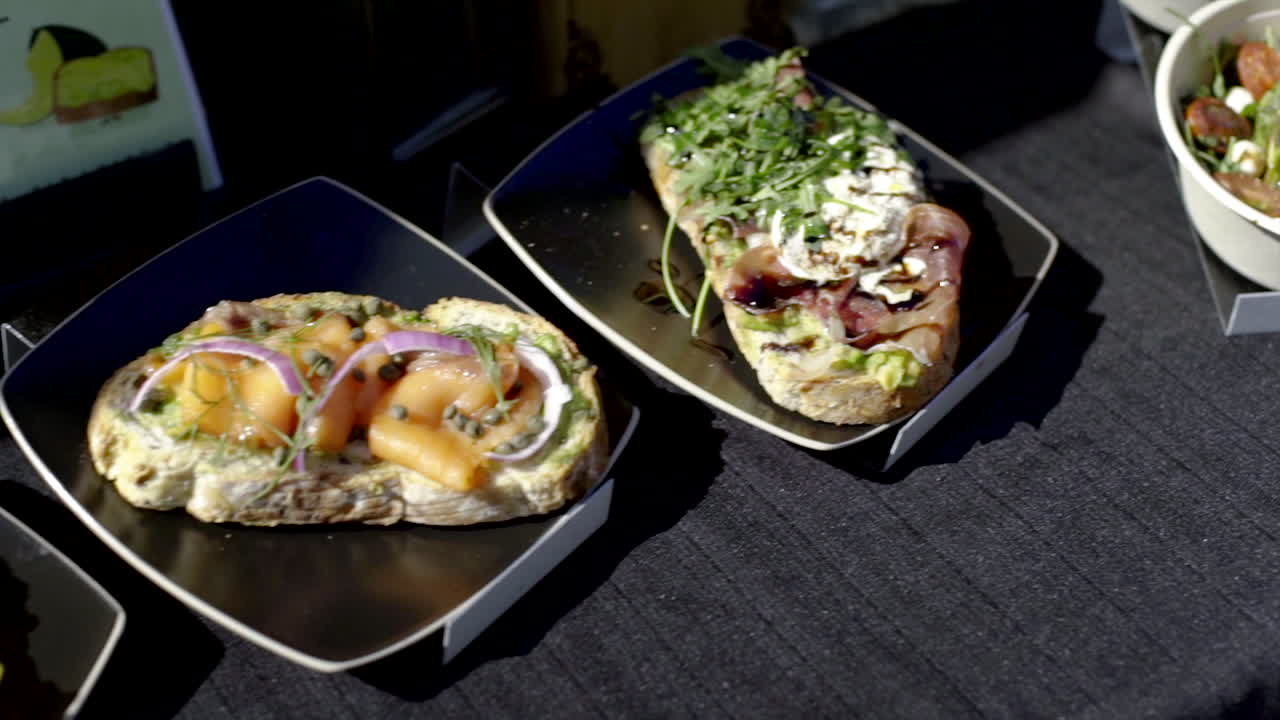 Close-up of various gourmet bruschetta on black plates, featuring ingredients like salmon, prosciutto, and cheese