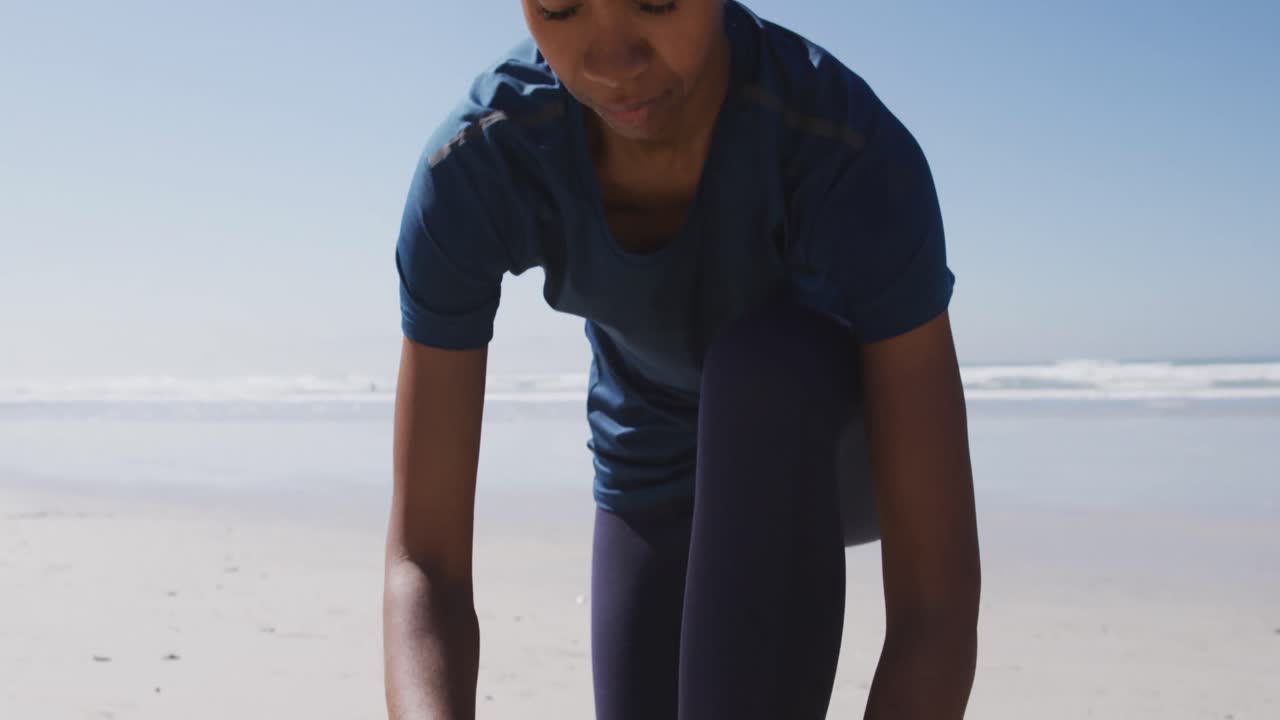 mujer afroamericana atando su zapato en la playa y el fondo del cielo azul