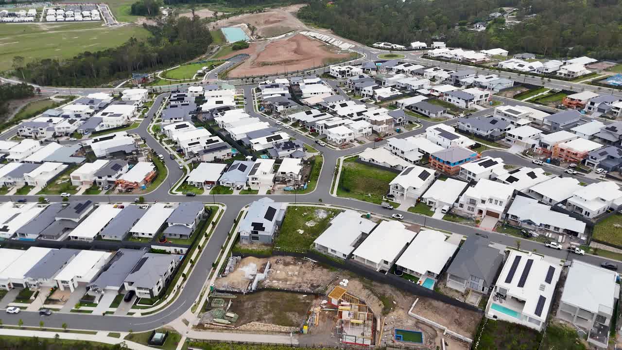 Drone glides above new residential neighborhood, showing modern homes, green forest, and overcast daylight