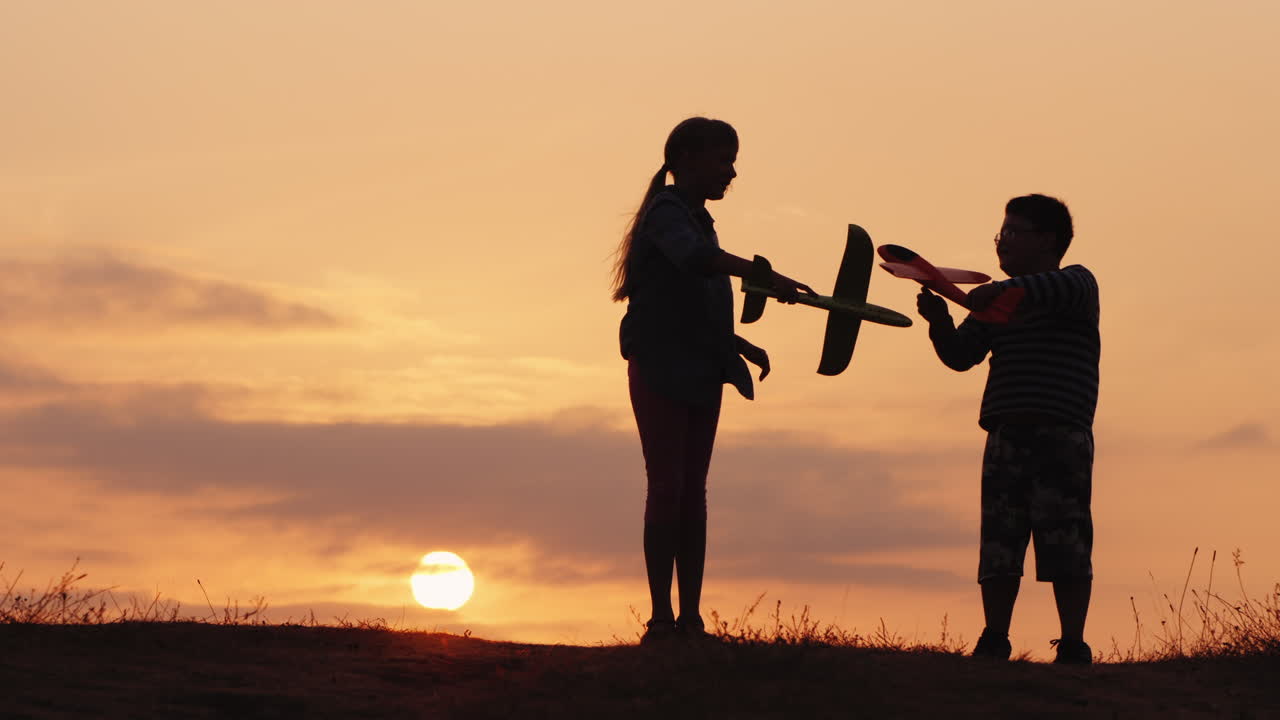 Sagome di una bambina e un bambino che giocano con gli aeroplani al tramonto. Bambini felici e spensierati.