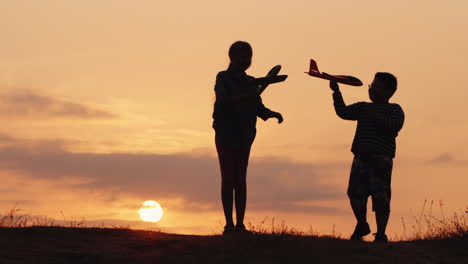 silhouettes of a girl and a boy playing together with airplanes at sunset a happy and carefree child